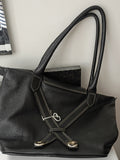 A black pebbled leather handbag with double top handles and a decorative crossed strap detail on the front